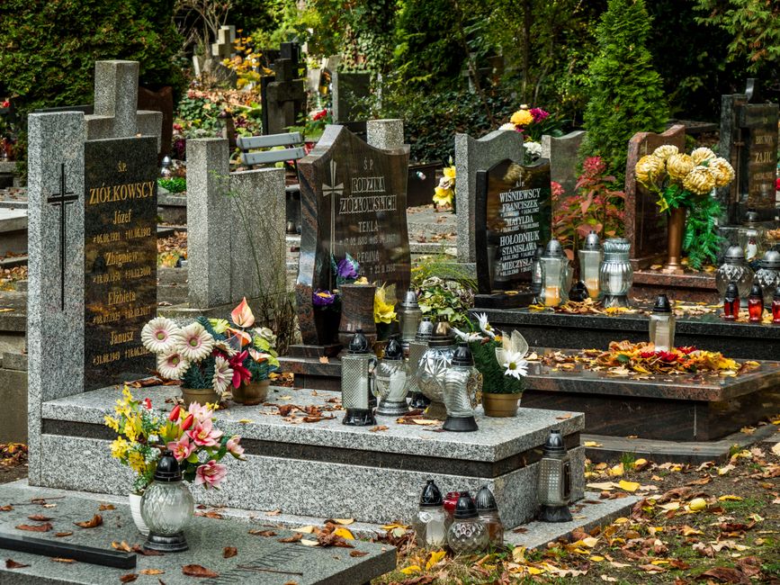 A collection of graves at Redhill Memorial Park adorned with floral tributes, including arrangements of white, pink, yellow, and purple flowers placed in vases and baskets. The headstones are made of 